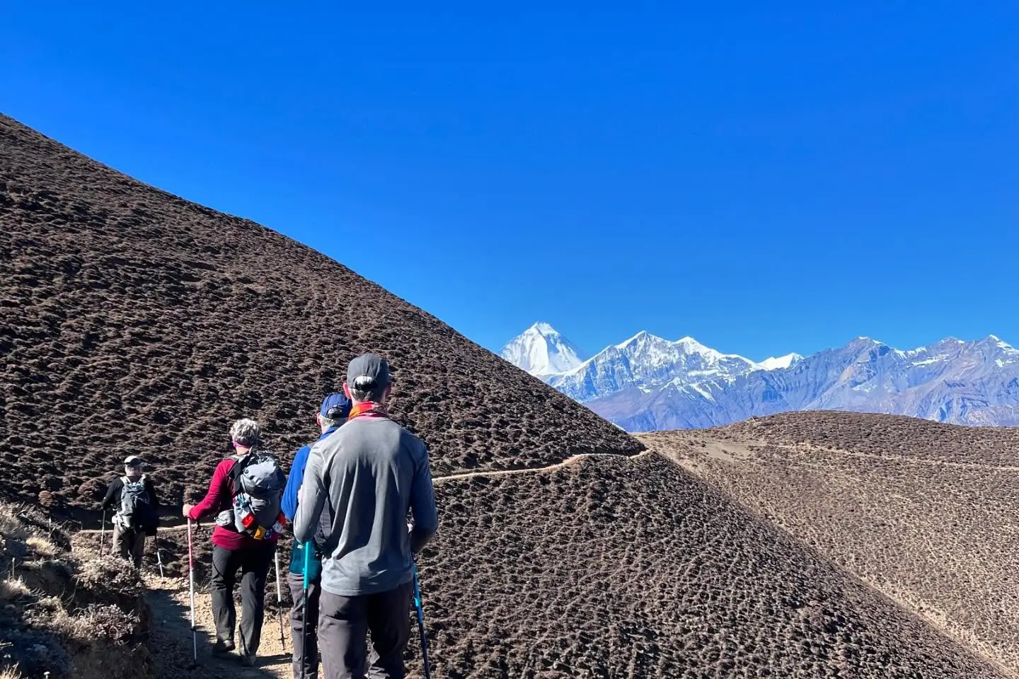 Trekkers cross high desert slopes with Dhaulagiri gleaming on the horizon